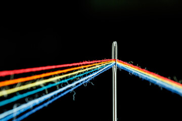Obraz premium multi-colored threads for sewing in the form of a rainbow pass through an antique needle on a black background