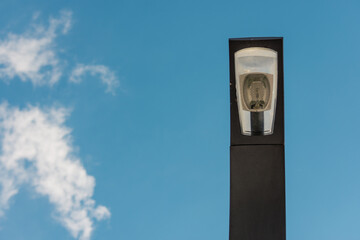 Close up to a black modern LED street light head with bulb against a cloudy sky