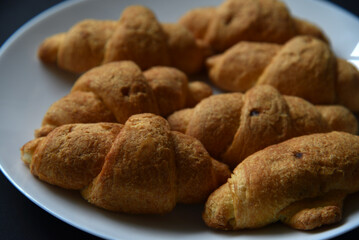 French croissants on a white plate. Delicious and sweet bread croissants. Sweet breakfast on a black background. European cuisine.
