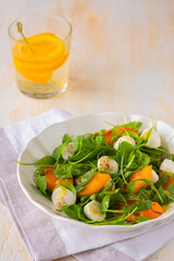 Healthy salad with arugula, slices of juicy persimmon and mozzarella in a beige ceramic plate on a light concrete background. Salad recipes.