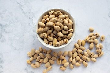Pistachio nuts in a bowl on white marble background. Close up, top view, copy space. Healthy snack
