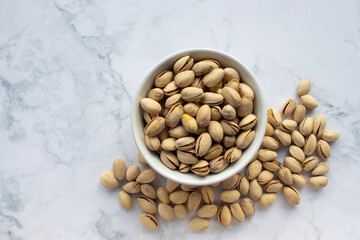 Pistachio nuts in a bowl on white marble background. Close up, top view, copy space. Healthy snack