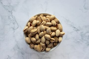 Pistachio nuts in a bowl on white marble background. Close up, top view, copy space. Healthy snack
