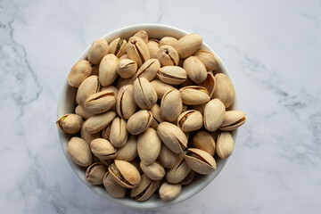 Pistachio nuts in a bowl on white marble background. Close up, top view, copy space. Healthy snack