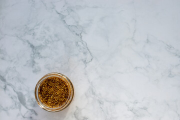 Fototapeta premium Mustard seeds sauce in glass jar on marble table background. Top view, copy space