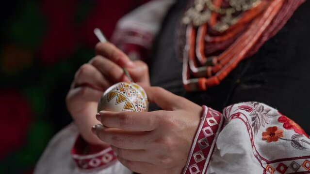 Ukrainian woman painting traditional ornamets on Easter egg - pysanka. Artist working in national costume. Preparation for Christian holiday