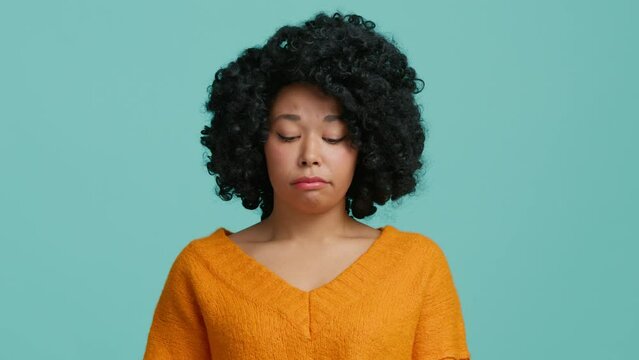 Fun confused shy shamed young African American woman girl 20s in orange clothes look camera bit lips, say oops i am sorry, Model feeling guilty isolated on pastel teal blue background.People lifestyle