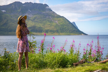 a long-haired girl in a colourful dress enjoys the sunny weather on the island of senja, norway,...