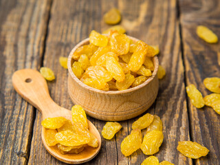 Golden dried raisins in a wooden bowl and spoon on an old wooden table.