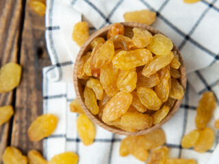 Golden dried raisins in a wooden bowl and spoon on an old wooden table.