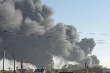 A large column of smoke rises above the houses and a road from an explosion of a Russian missile