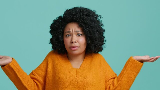 Young indifferent unsure African American woman makes gesture of I do not know, can not help anything. Difficult question facial expression lifestyle people concept. Blue studio isolated background 4K