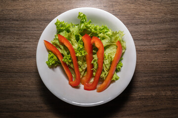 Plate with green lettuce leaves and strips of red pepper on a wooden kitchen worktop