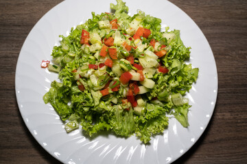Homemade salad with green lettuce leaves, spring onions, cucumber and red peppers on a wooden kitchen top