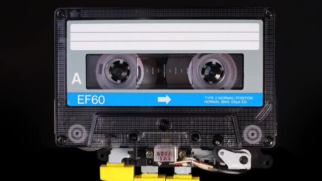 Audio cassette tape in use for sound recording in a tape recorder. A vintage blue color, brand new blank labelled music cassette playing back in a deck player. Static video camera shot. Close up 4K
