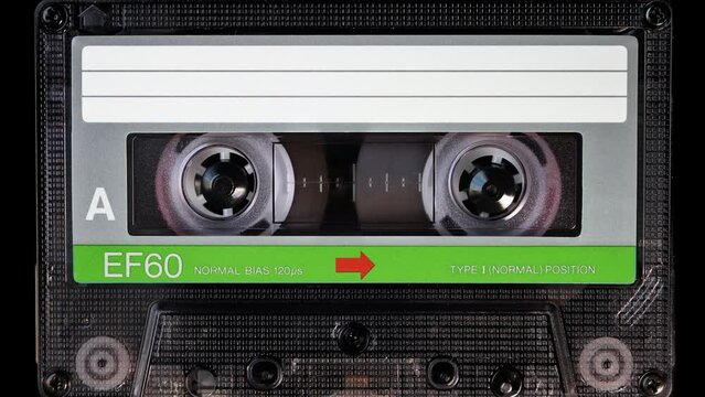 A vintage green colored brand new blank labelled music cassette playing back in a deck player. Audio cassette tape in use for sound recording in a tape recorder. Static video camera shot. Close up
