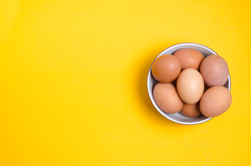 Brown chicken eggs on yellow background in a white bowl. Easter and healthy eating.
