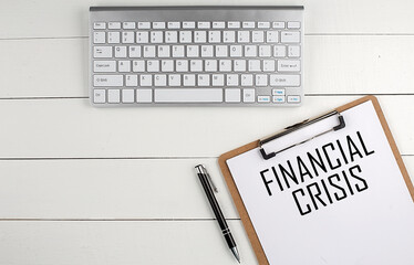 Home office workspace with keyboard, clipboard and pen with text FINANCIAL CRISIS on white wooden background , business concept