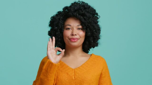 Cheerful funny young African American girl with afro hairstyle, noddle and showing OK sign with fingers. Everything is OK sign hand gesture, Agreement expression. Young girl isolated studio background