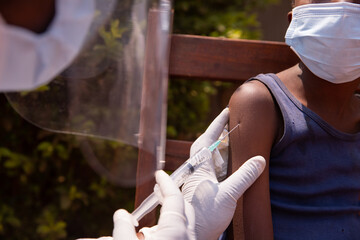 Young toddler wearing a face mask sitting outdoor taking his vaccine on a shoulder