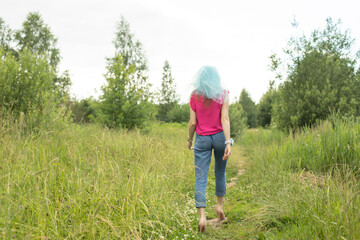 Naklejka na ściany i meble Girl walking on grass. Beautiful woman goes into distance. Jeans and veil on his head.