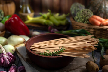 dry noodles in wooden bowl on table full of fresh vegetables squash peppers garlic bell peppers fresh eggs artichokes onions with wooden background