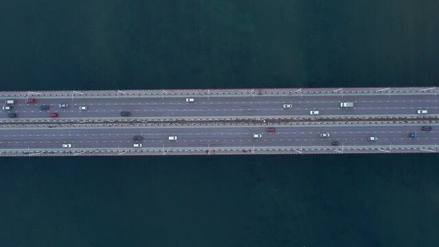 4k Top view of cars drive on bridge over waters outdoors irrl. Aerial of transport riding asphalt road surrounded by blue sea or river on summer day. Amazing drone picture of traffic and modern