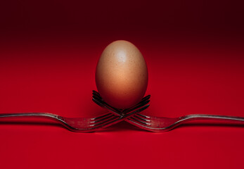 graphic composition of an egg placed on two crossed forks with a red background