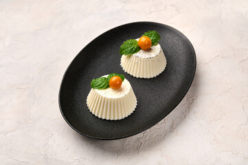Homemade two panna cotta with natural vanilla pod, physalis or winter cherry and mint on black oval...