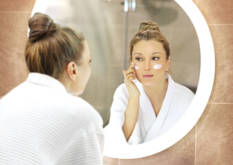 woman looking in the mirror in the bathroom and taking care of her skin.Applying the cream	.Magic anti-aging cream.