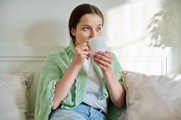 Adolescent girl resting with cup of hot tea, sitting on couch at home