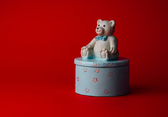 small round jewelry box with a small teddy bear on the lid, the whole placed on a red background