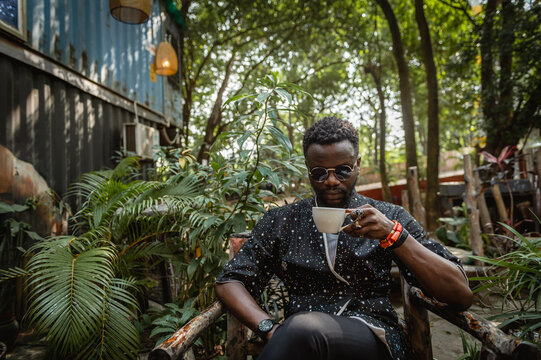 a black man holding in tea cup in a garden 