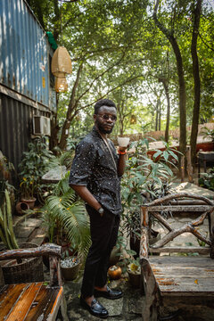 black man standing and holding a tea cup in a garden