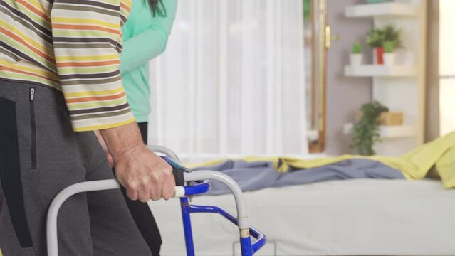 A senior man using a walker in a rehab center or nursing home.
Patient walking with walker and female nurse helping him.
