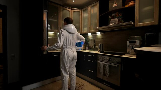 An astronaut in the kitchen is looking for something to eat in the refrigerator. The concept of a real everyday life of an astronaut in his ordinary apartment.
