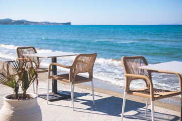 Fototapeta na wymiar Restaurant terrace by the sea, seaside view cafe on the beach, empty chairs and tables Ionian sea shore, Greece, blue sea with crystal clear water