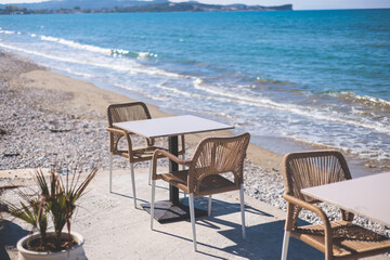 Restaurant terrace by the sea, seaside view cafe on the beach, empty chairs and tables Ionian sea shore, Greece, blue sea with crystal clear water