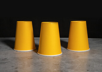 Three inverted yellow paper disposable cups. The concept of cheating, fraud, gambling.
