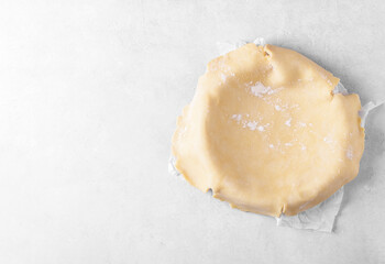 Raw crust pie dough into a baking dish on a light gray background. Top view of homemade pie crust on the table. Home baking concept, pie crust recipe, hobby home bakery, copy space