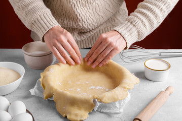 Woman arranging the dough in the pie pan on the table in the kitchen. Authentic female hands are putting homemade crust pie dough into a baking dish. Making a base for a shortcrust pie, apple pie