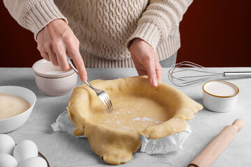 Woman using fork to poke the holes all over the dough on the table in the kitchen before baking homemade pie crust. Authentic female hands making a base for a shortcrust pie, pie crust recipe