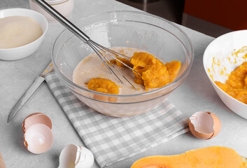 Bowl with pumpkin pie filling and whisk with ingredients for baking a pie on a gray table in the kitchen. Home cooking concept, traditional pumpkin pie recipe