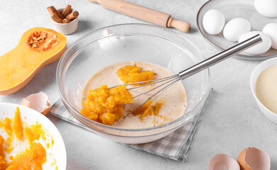 Bowl with pumpkin pie filling and whisk with ingredients for baking a pie on a gray table in the kitchen. Home cooking concept, traditional Thanksgiving pumpkin pie recipe, close up