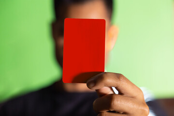 
Hombre mostrando tarjeta roja o amarilla en fondo verde concepto de árbitro futbol o deporte en general. Amonestación deportiva.
