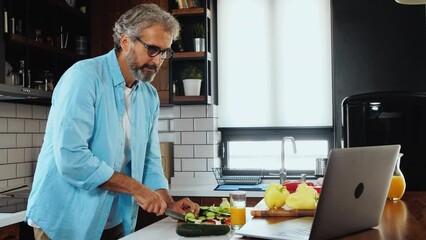 Senior man in kitchen watching laptop - Powered by Adobe