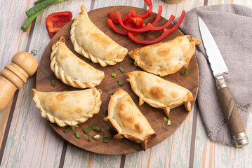 Homemade chicken and meat empanadas with different repulgue on a wooden plate with pepper and oil can with fresh vegetables