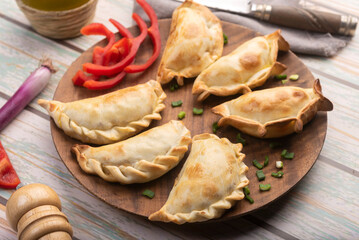 Homemade chicken and meat empanadas with different repulgue on a wooden plate with pepper and oil...