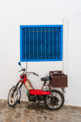 Old red motorcycle with a crate standing under blue window in Sidi Bou Said village near Carthage...
