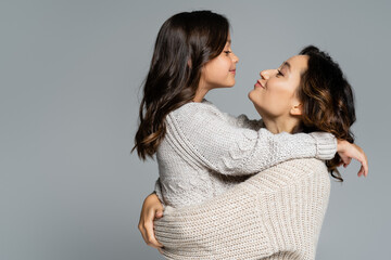 side view of positive woman and girl in autumn knitwear looking at each other isolated on grey